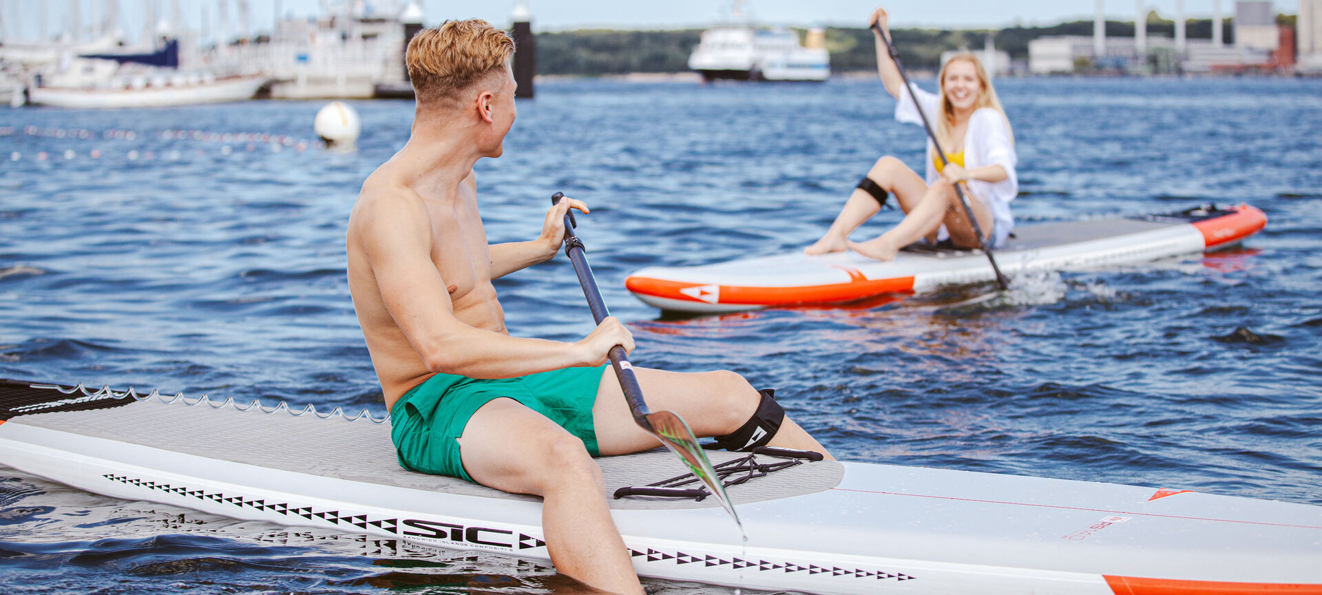 Man und Frau sitzen jeweils auf einem SUP Board in der Kieler Förde